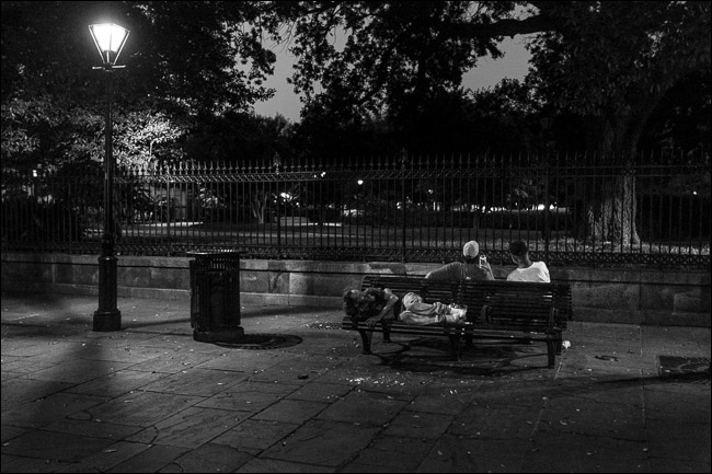dwóch mężczyzn siedzących w nocy na ławce w parku;  jeden mężczyzna śpi na siedzeniu za nimi