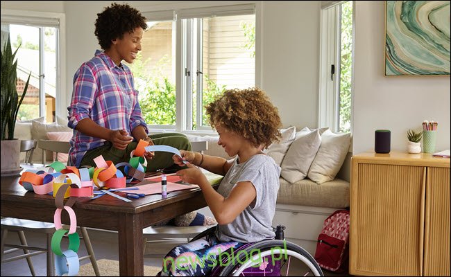 Małe dziecko na wózku inwalidzkim robi rękodzieło z mamą przy stole z Amazon Echo w pobliżu.