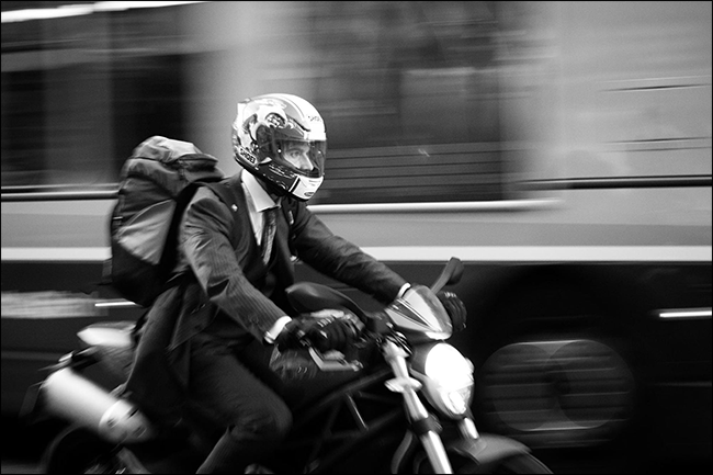 mężczyzna w garniturze na motocyklu z niewyraźnym autobusem jadącym za nim