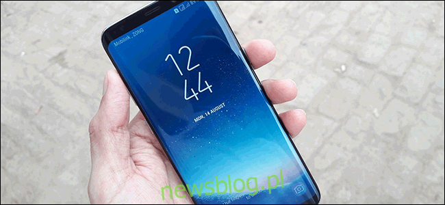 Dłoń trzymająca Samsunga Galaxy S8 z ekranem dotykowym pokazującym godzinę i datę.