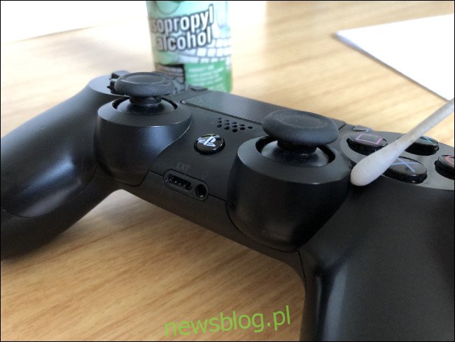 Kontroler DualShock 4 z końcówką Q na górze obok butelki z alkoholem izopropylowym.