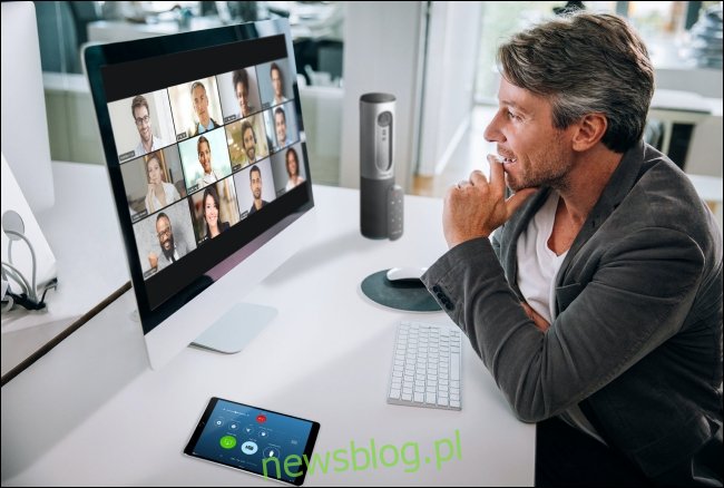 Mężczyzna na spotkaniu Zoom na swoim Macu z uczestnikami w widoku galerii na monitorze. 