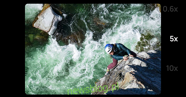 Powiększone ujęcie mężczyzny na linie wspinającego się po skałach obok rwącej rzeki. 