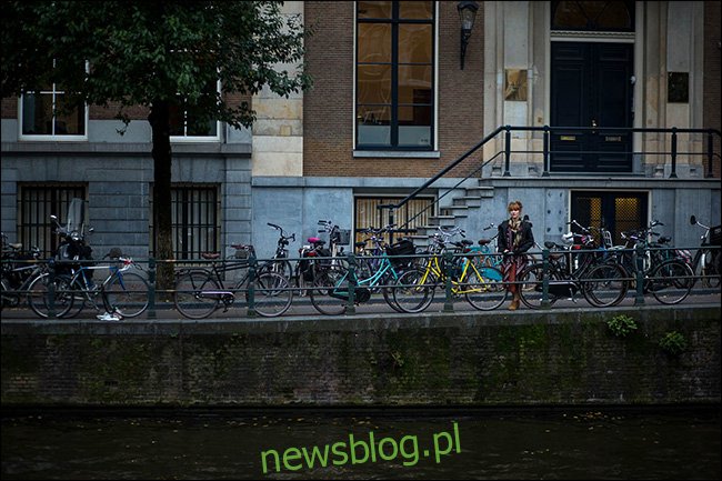 Kobieta stojąca na moście za linią zaparkowanych rowerów.