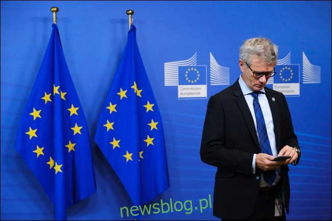 Mężczyzna używający smartfona z dwoma flagami UE za sobą.