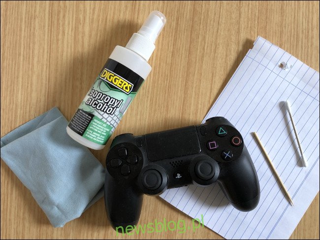 Kontroler DualShock 4 znajdujący się na kawałku papieru obok wykałaczki, końcówki Q, butelki z rozpylaczem alkoholu izopropylowego i szmatki. 