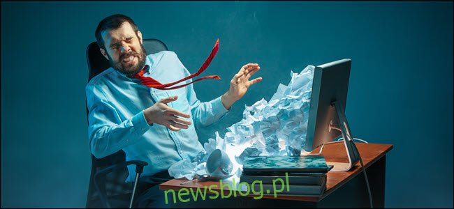 Młody podkreślił przystojny biznesmen pracuje przy biurku w nowoczesnym biurze krzycząc na ekranie laptopa i zły na spam e-mail.  Kolaż z górą pomiętego papieru.