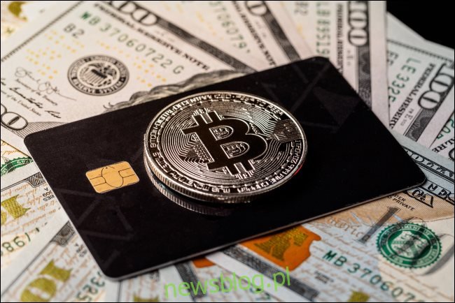 Fizyczny token Bitcoin na karcie kredytowej leżącej na banknotach o wartości 100 USD.
