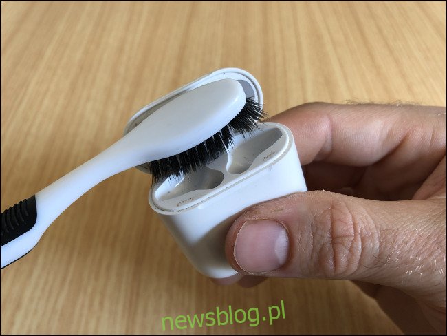 Dłoń trzymająca etui Apple AirPods i czyszcząca je szczoteczką do zębów.
